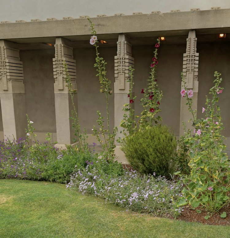 Green grass, brown mulch and pink, red, white, and purple flowers in front of sand colored columns